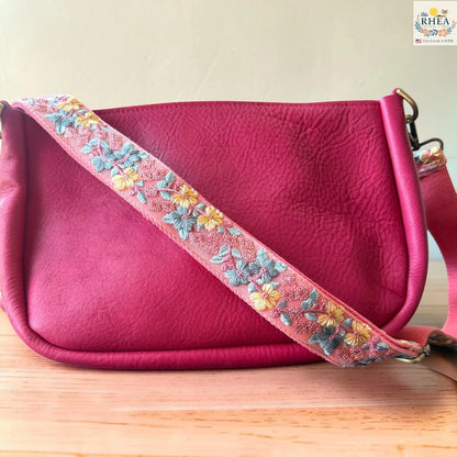 Rhea Artistry Studio blush pink crossbody strap with yellow floral and turquoise leaf embroidery, 1.5-inch width, adjustable length.
