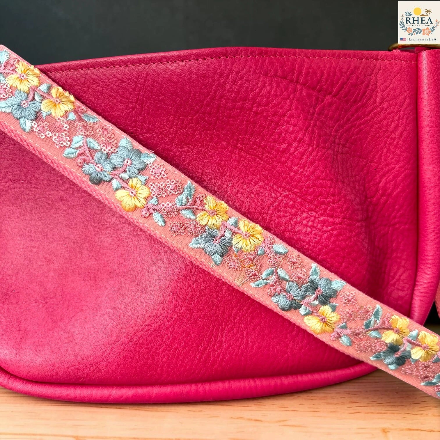  Rhea Artistry Studio coral pink crossbody strap with yellow floral and turquoise leaf embroidery, 1.5-inch width, adjustable length.