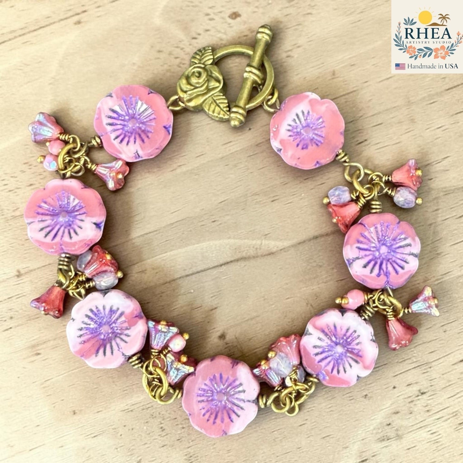 Rhea Artistry Studio handmade bracelet with pink glass flower beads, purple centers, and antique brass toggle clasp with floral detail.