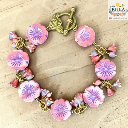 Rhea Artistry Studio handmade bracelet with pink glass flower beads, purple centers, and antique brass toggle clasp with floral detail.
