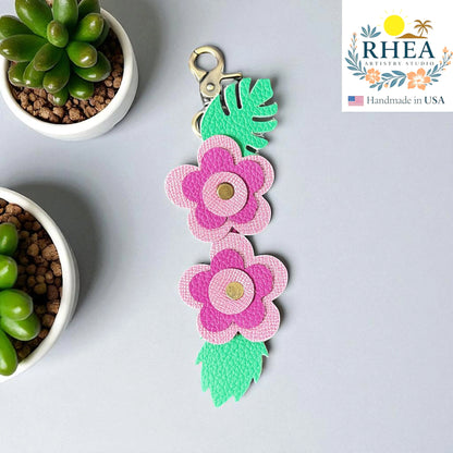 Rhea Artistry Studio handmade pink and purple leather floral keychain with green leaf accents and gold center detail.