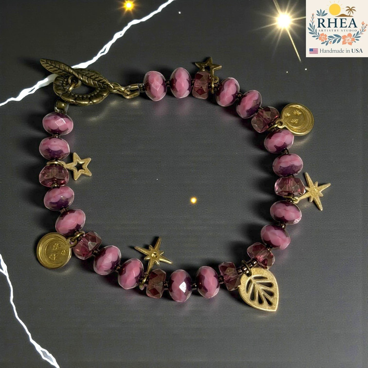 Rhea Artistry Studio pink glass bead bracelet with brass celestial charms and floral toggle clasp.