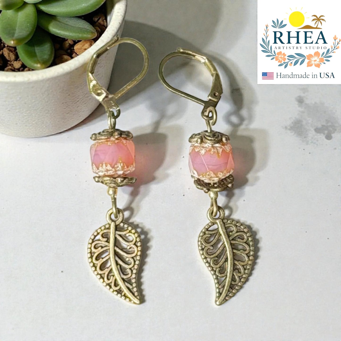 Rhea Artistry Studio pink faceted glass bead and antique brass leaf drop earrings, 2 inches long.