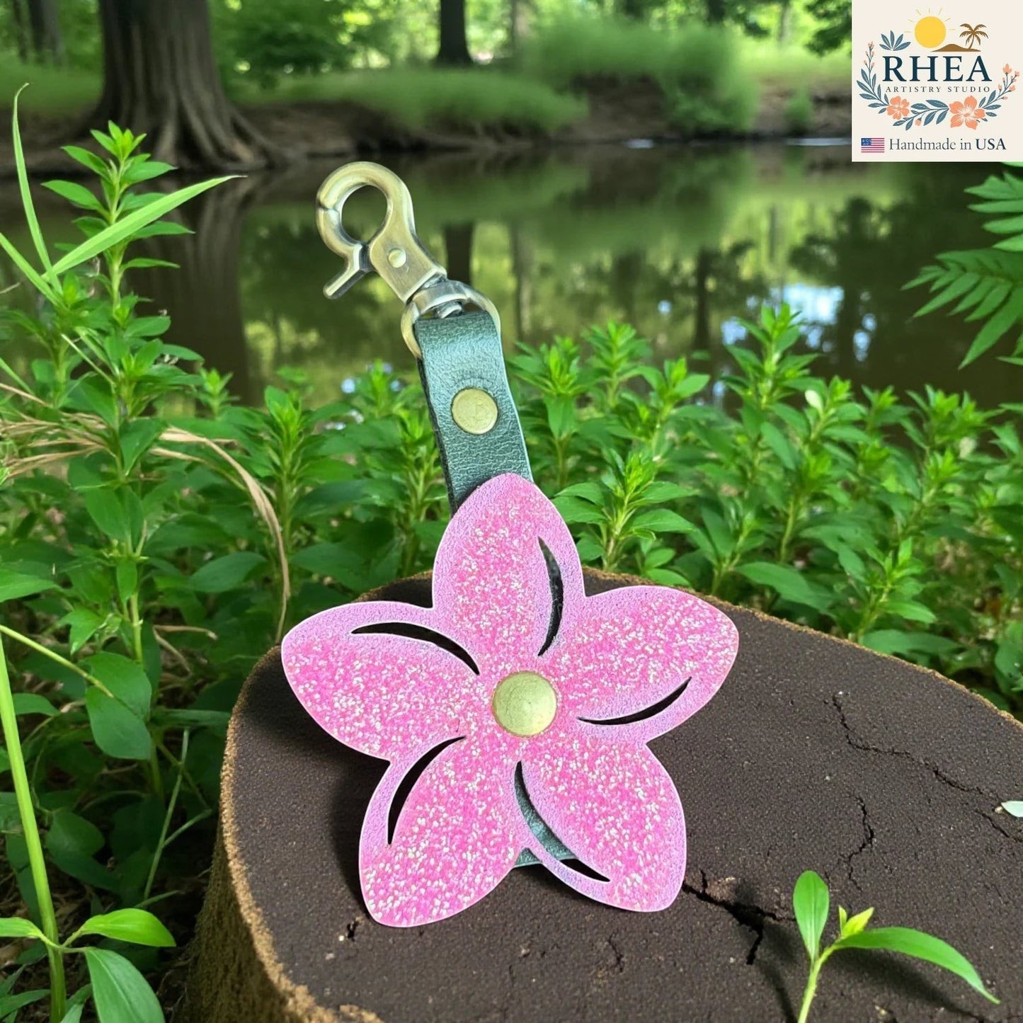 Rhea Artistry Studio pink glitter leather plumeria flower bag charm with brushed brass hardware and green leather strap.