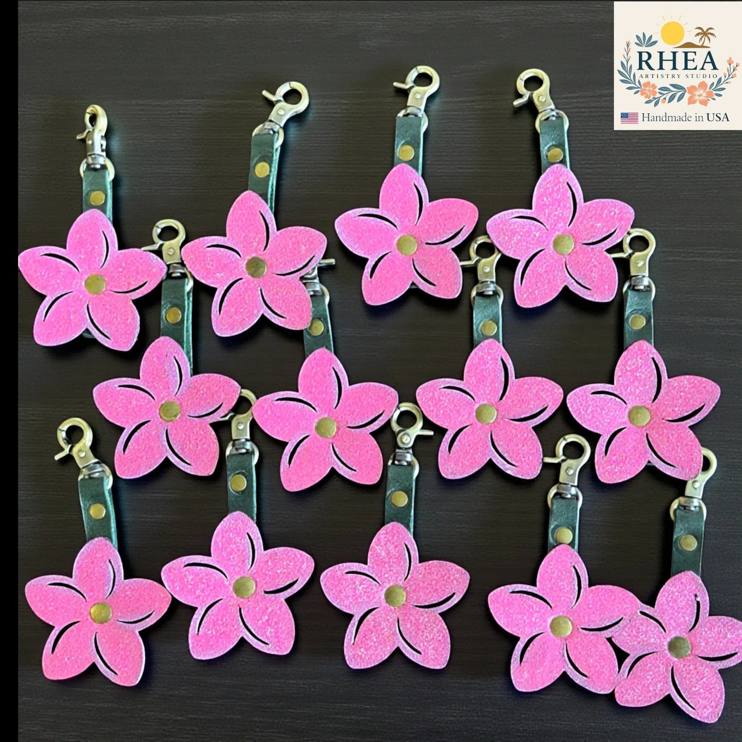 Rhea Artistry Studio pink glitter leather plumeria flower bag charm with brushed brass hardware and lobster clasp.