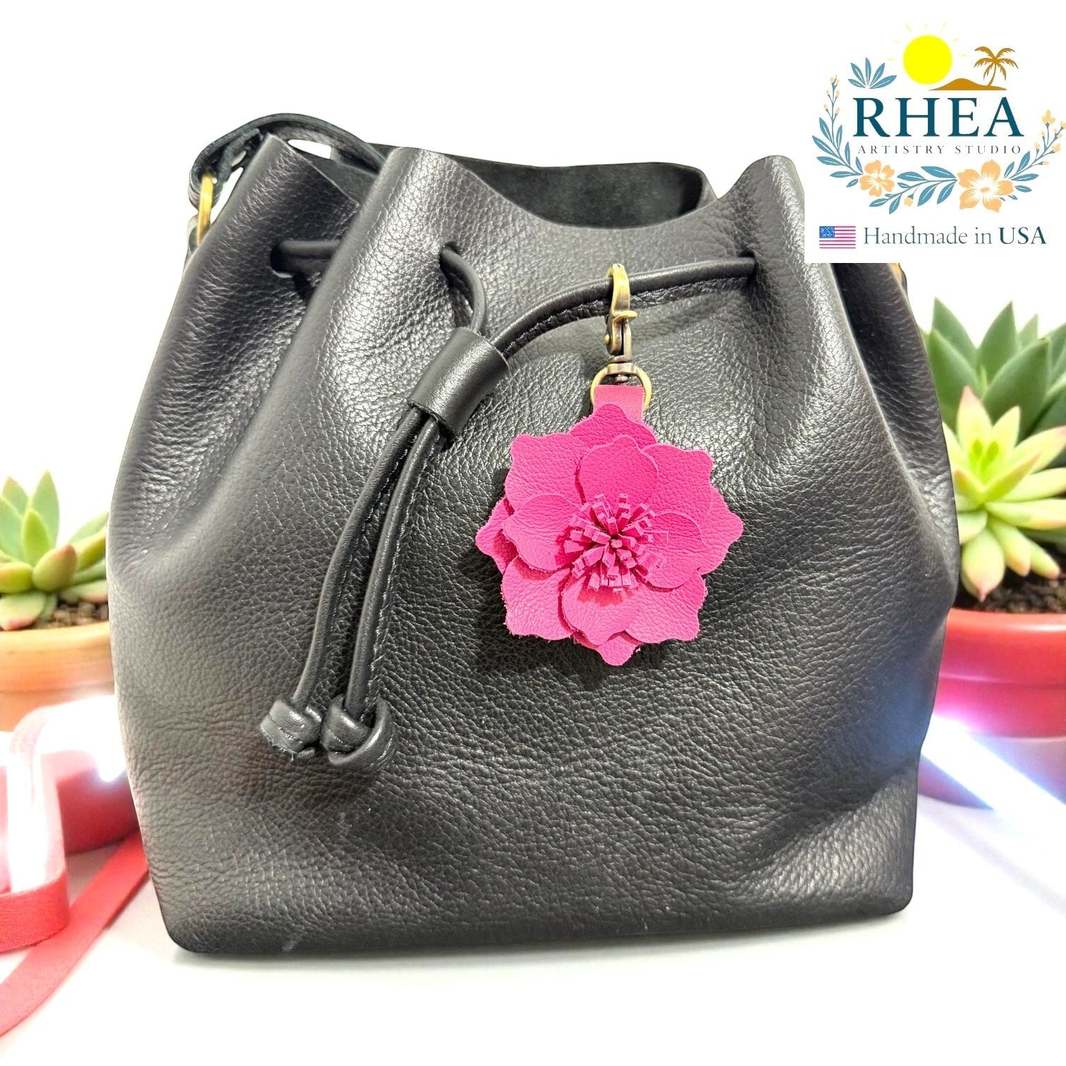 Rhea Artistry Studio bright pink leather flower charm attached to a black leather drawstring bag.