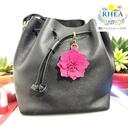 Rhea Artistry Studio bright pink leather flower charm attached to a black leather drawstring bag.