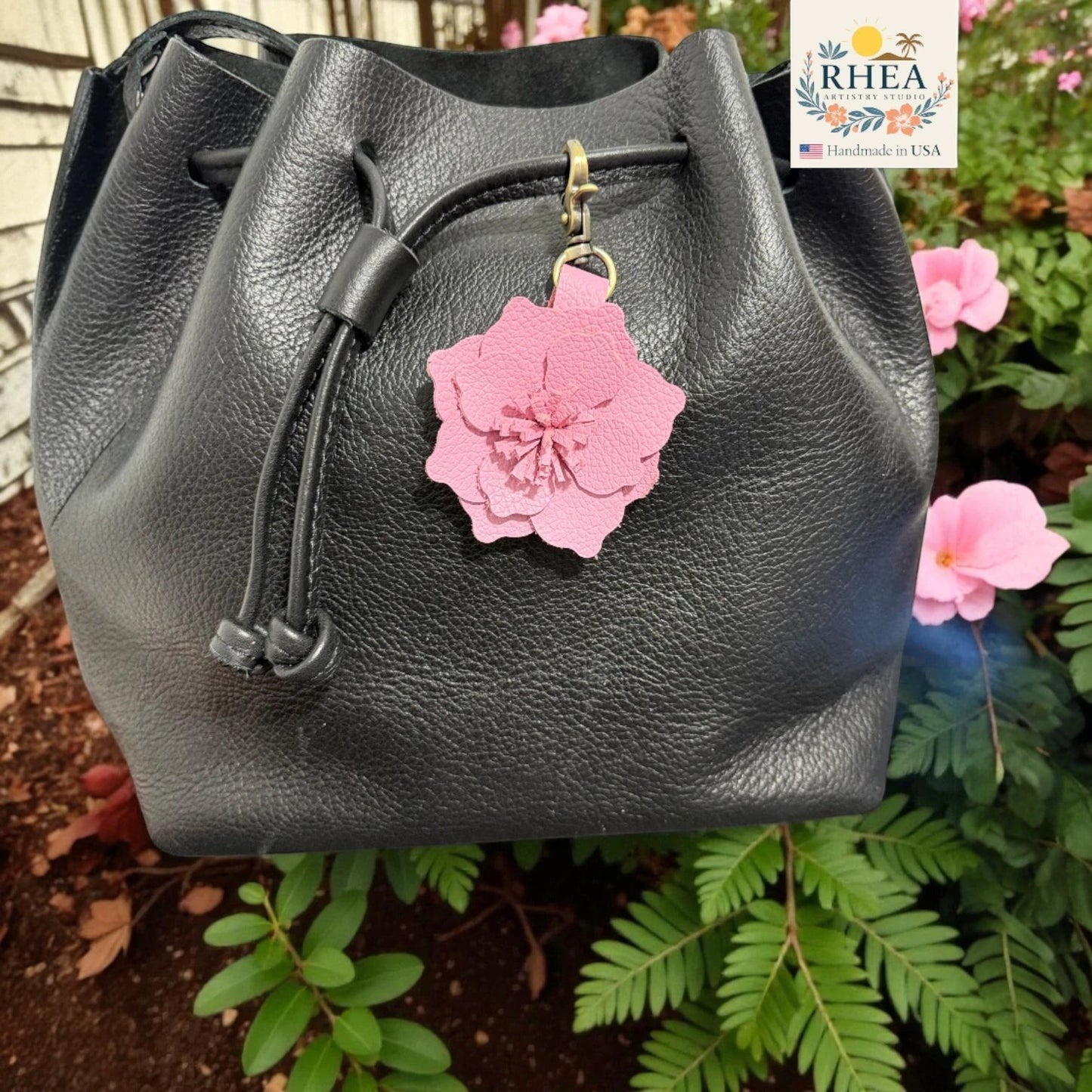 Rhea Artistry Studio pink leather flower charm attached to a black leather drawstring bag.