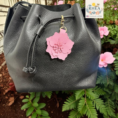 Rhea Artistry Studio pink leather flower charm attached to a black leather drawstring bag.