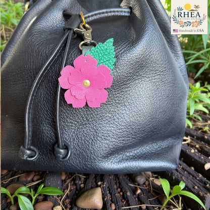Rhea Artistry Studio pink layered leather rose charm with green engraved leaf detail on a black leather bag.