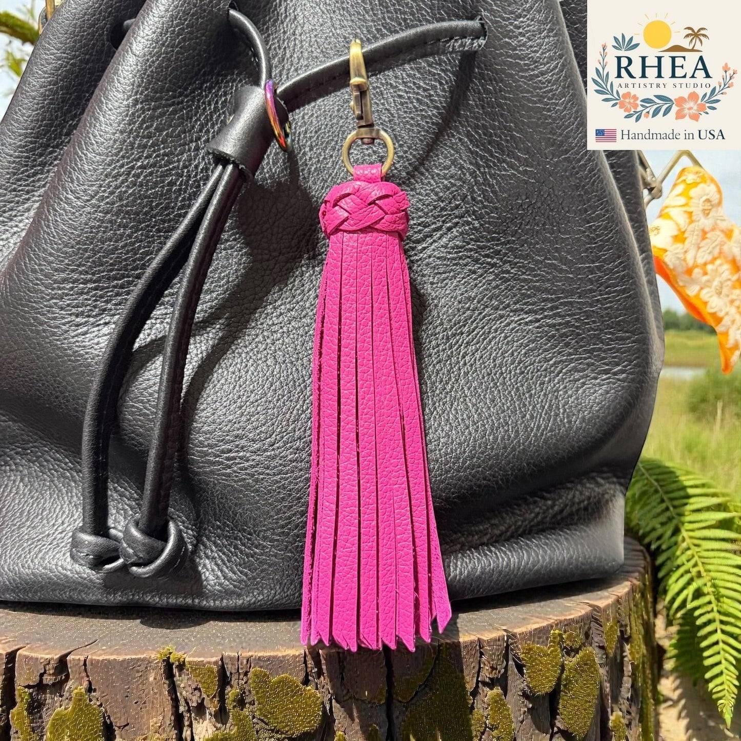 Rhea Artistry Studio bright pink leather tassel bag charm with braided detail and brass clasp, attached to a black leather bag.