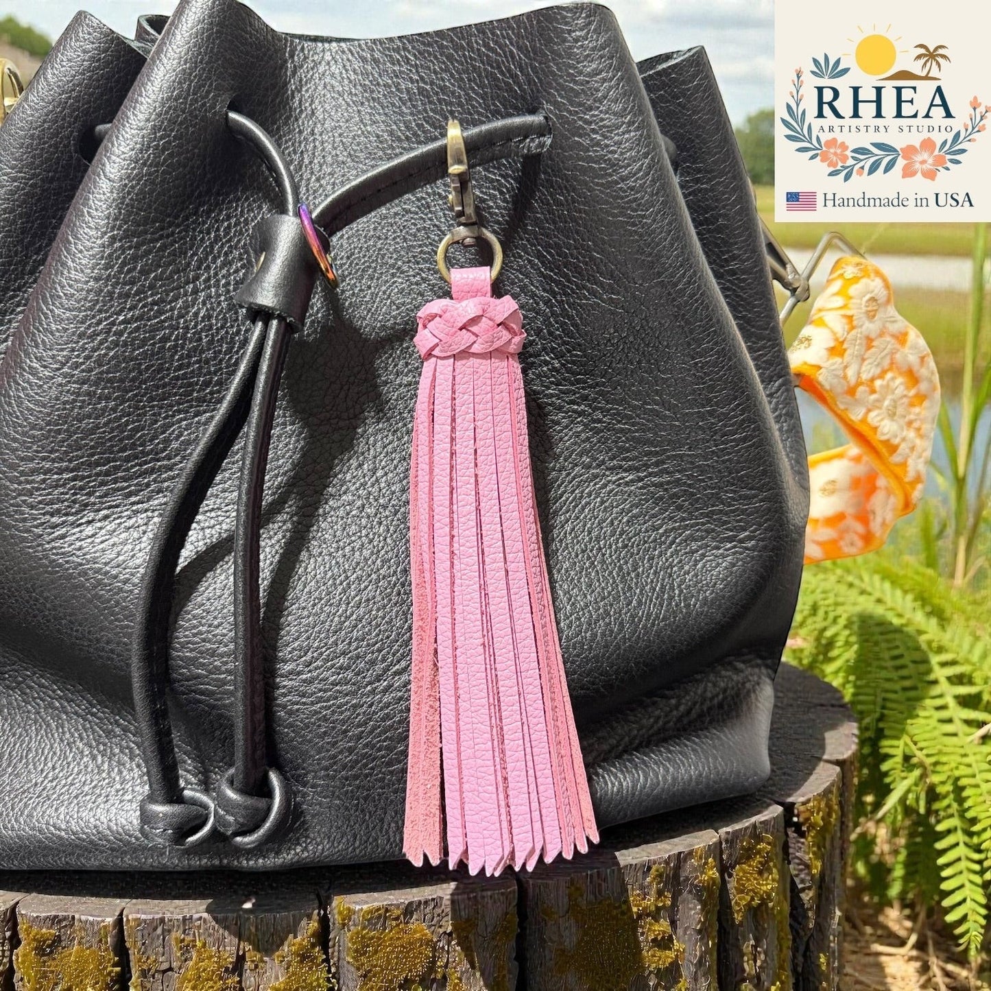 Rhea Artistry Studio pink leather tassel bag charm with braided detail and brass clasp, attached to a black leather bag.