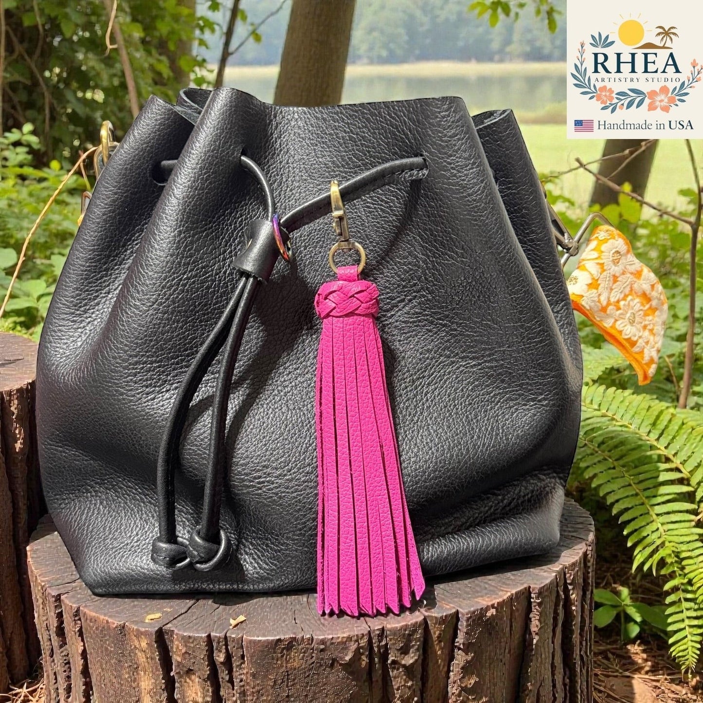 Rhea Artistry Studio bright pink leather tassel bag charm with braided detail and brass clasp on a black leather bag.