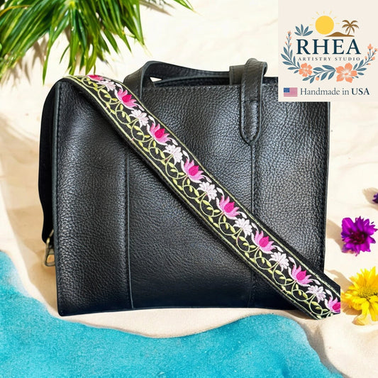 Rhea Artistry Studio black leather crossbody bag with a 1.5-inch adjustable strap featuring pink lotus embroidery and brushed brass hardware.