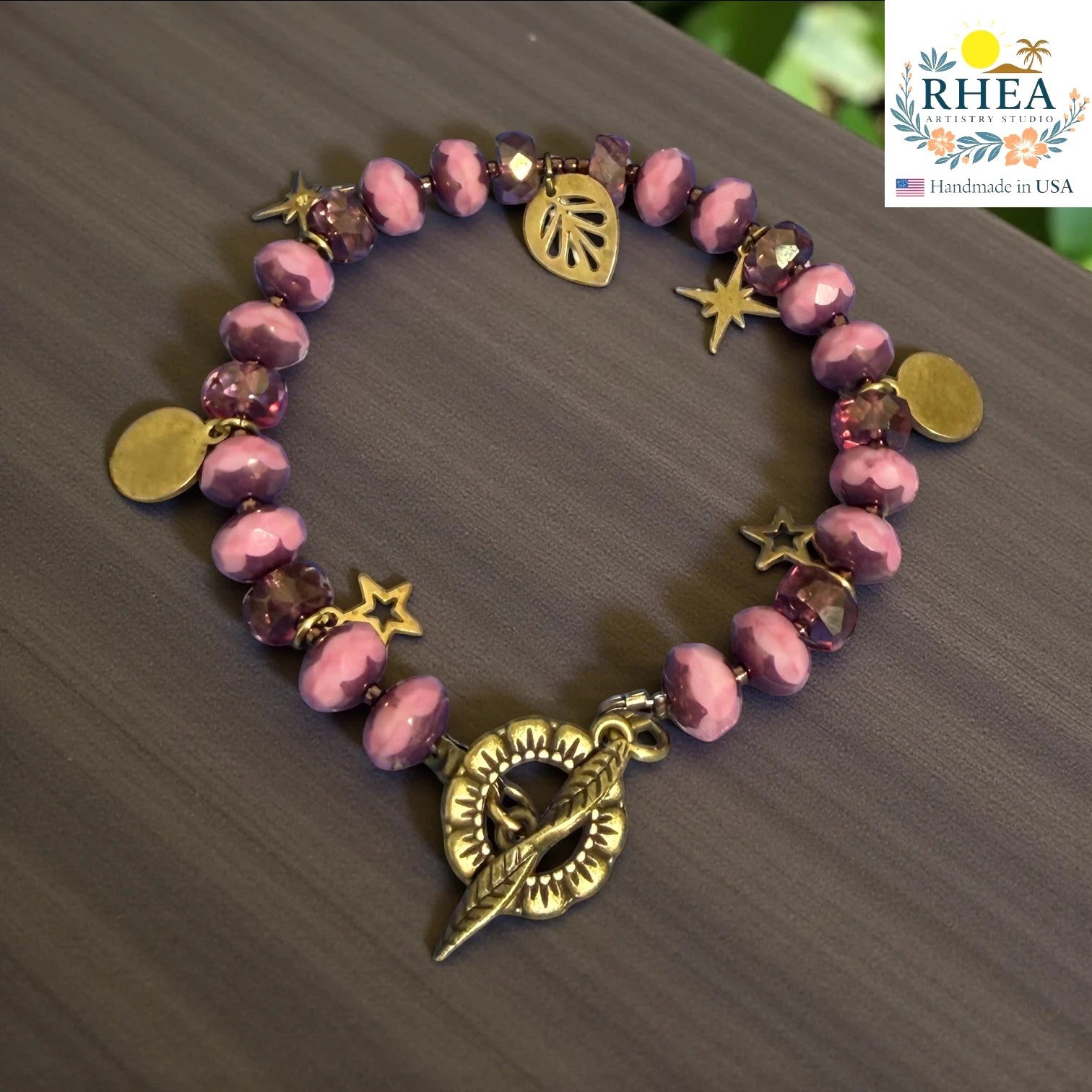Rhea Artistry Studio handmade purple glass bead bracelet with brass celestial charms and floral toggle clasp.