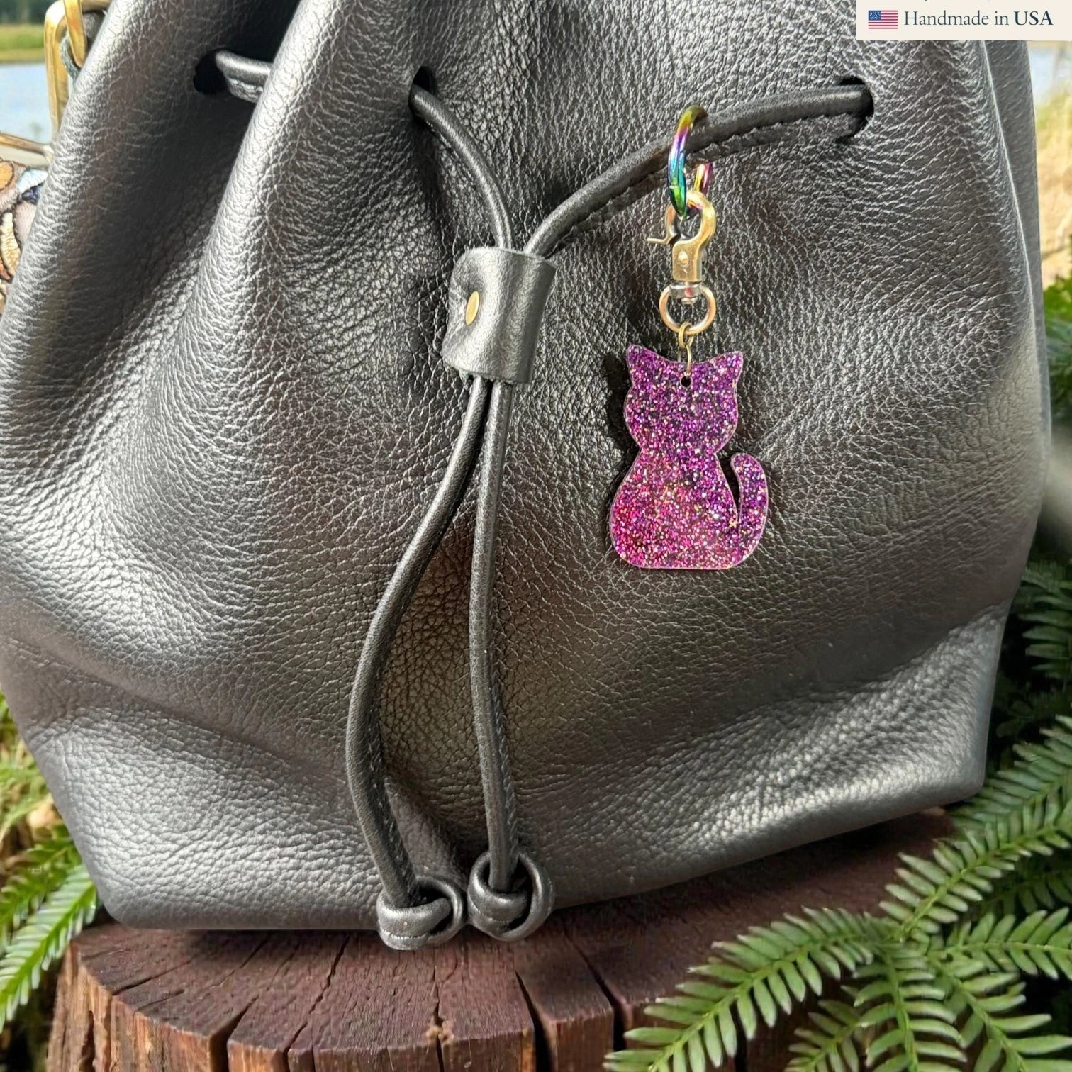 Rhea Artistry Studio purple glitter cat silhouette acrylic charm with antique brass clasp on a black leather bag.