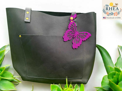 Rhea Artistry Studio purple leather butterfly charm with metallic iridescent finish attached to a black tote bag.