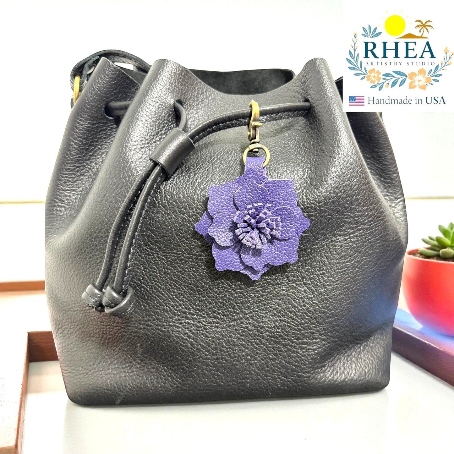 Rhea Artistry Studio purple leather flower charm attached to a black leather drawstring bag.