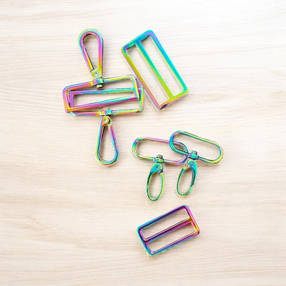 Rhea Artistry Studio rainbow iridescent metal hardware set including swivel clasps and strap adjusters for bags and straps.