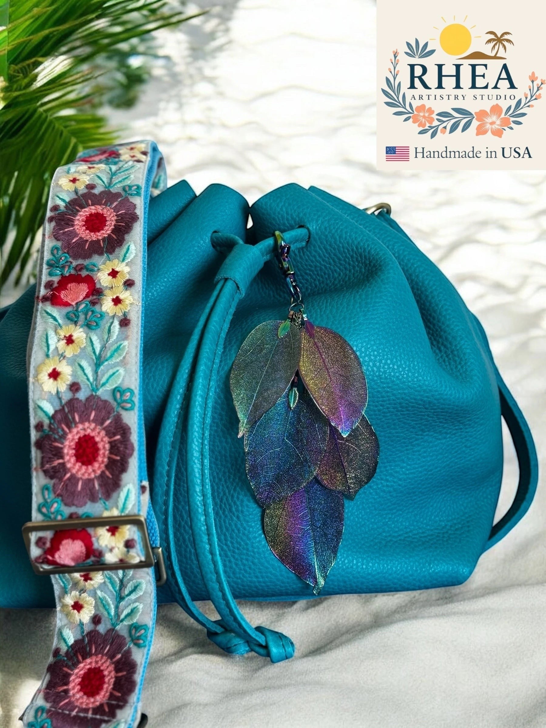 Rhea Artistry Studio handmade rainbow metallic electroplated real leaf bag charm on a teal drawstring bag.