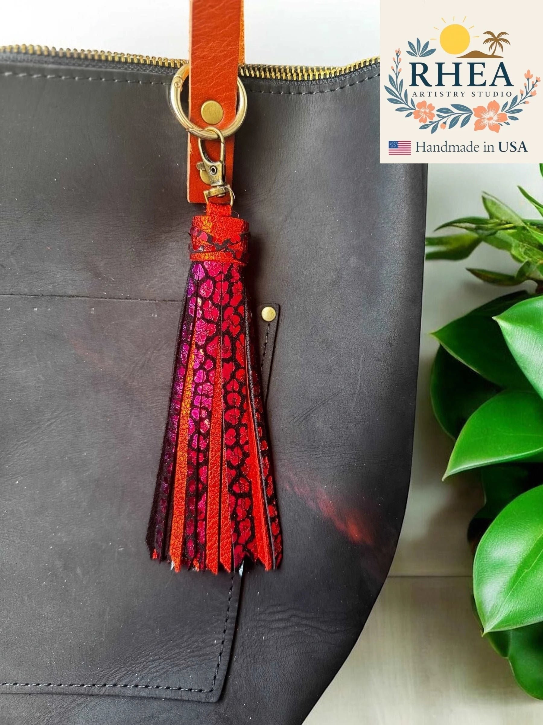 Rhea Artistry Studio handmade 7-inch rainbow chameleon leather tassel keychain with lobster clasp attached to a black tote bag.