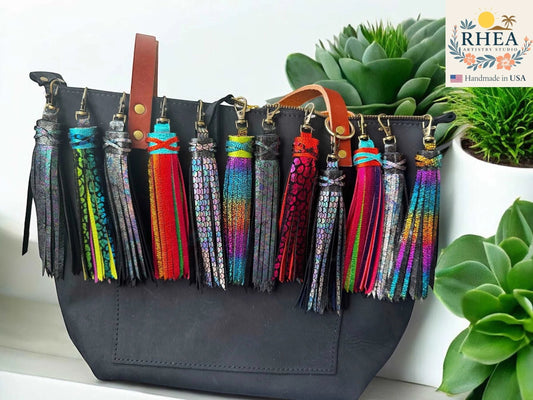 Rhea Artistry Studio handmade 7-inch rainbow chameleon leather tassel keychain with lobster clasp attached to a black tote bag.