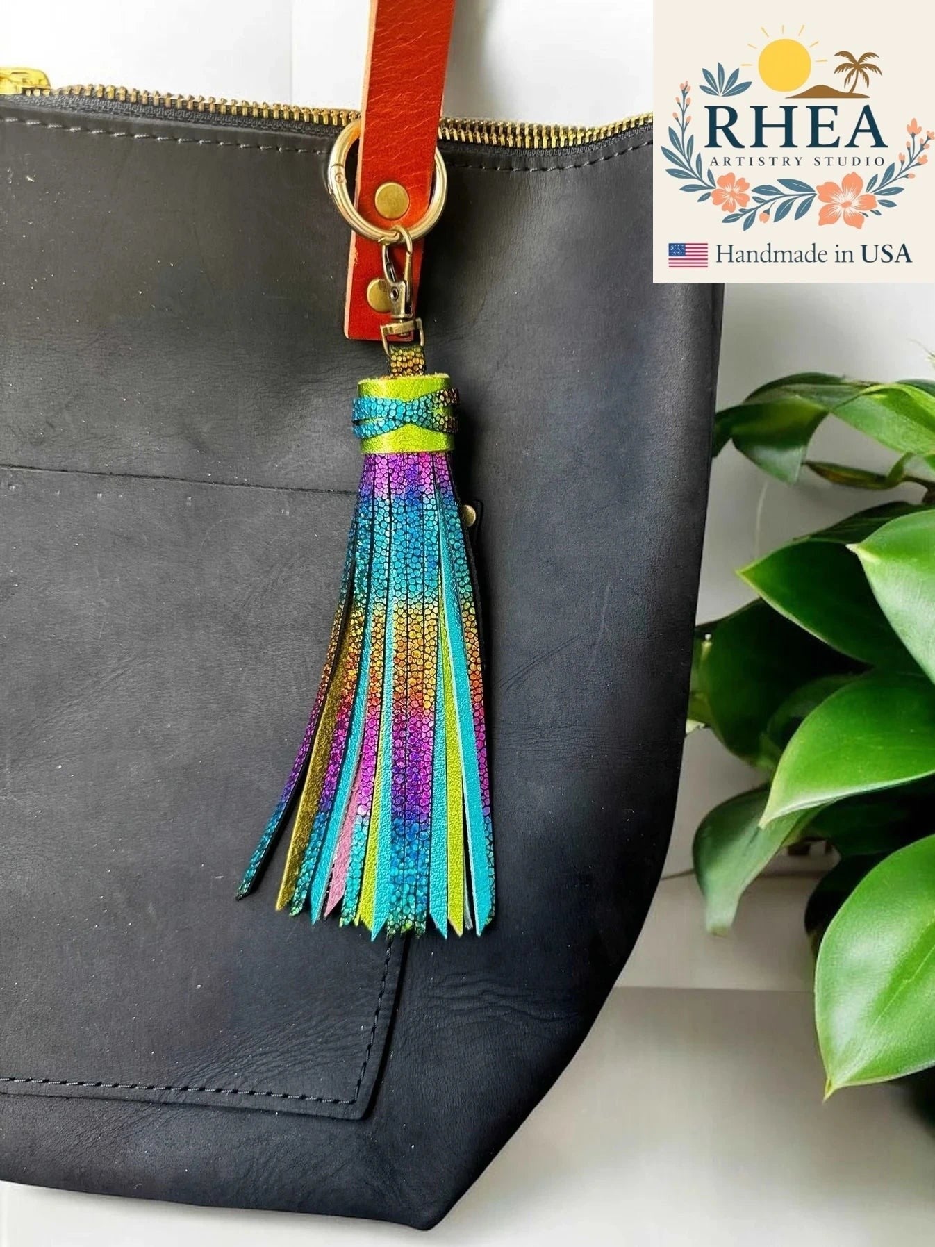 Rhea Artistry Studio handmade 7-inch rainbow chameleon leather tassel keychain with lobster clasp attached to a black tote bag.