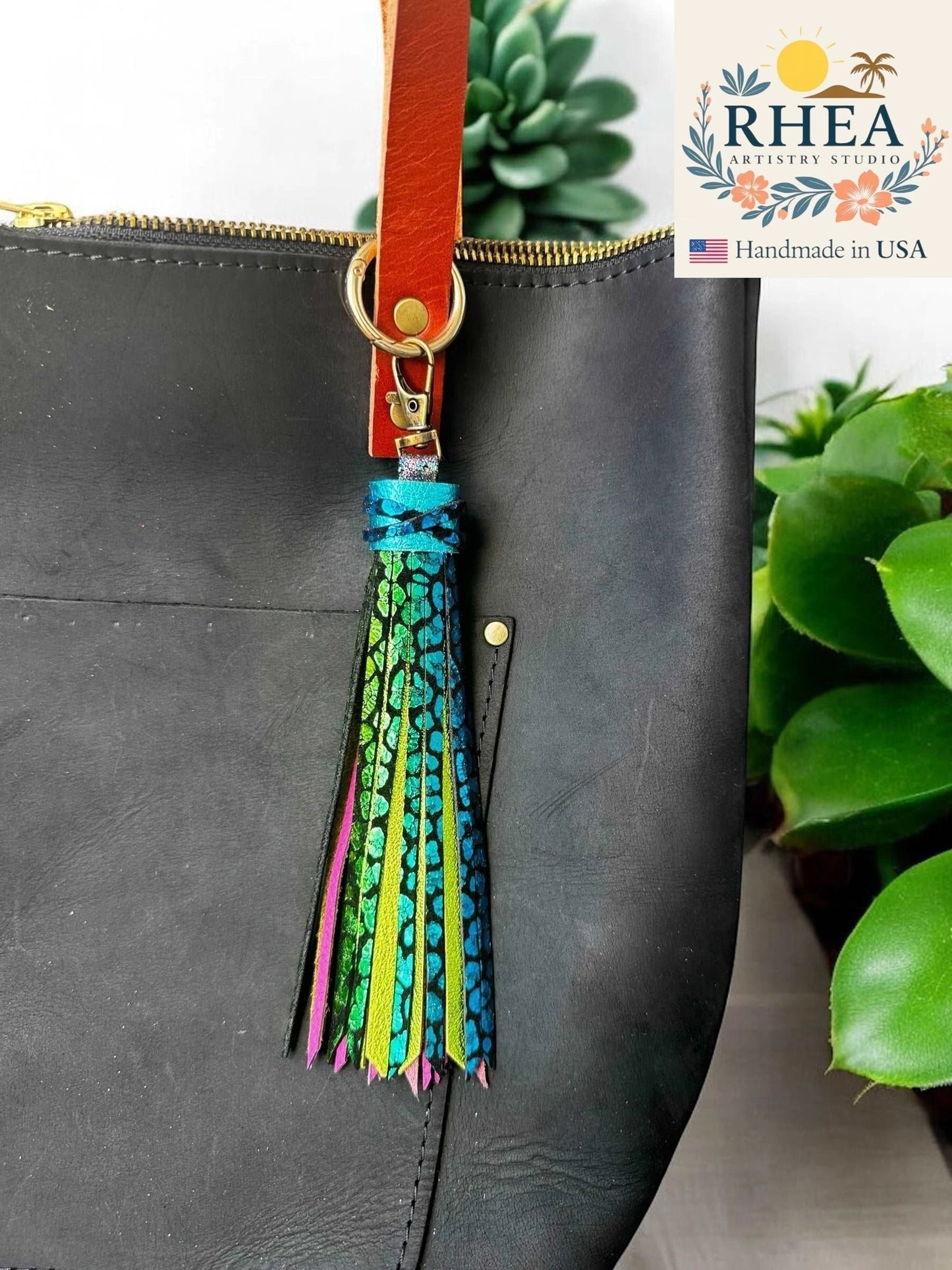 Rhea Artistry Studio 7-inch rainbow chameleon leather tassel keychain with lobster clasp attached to a black leather bag.