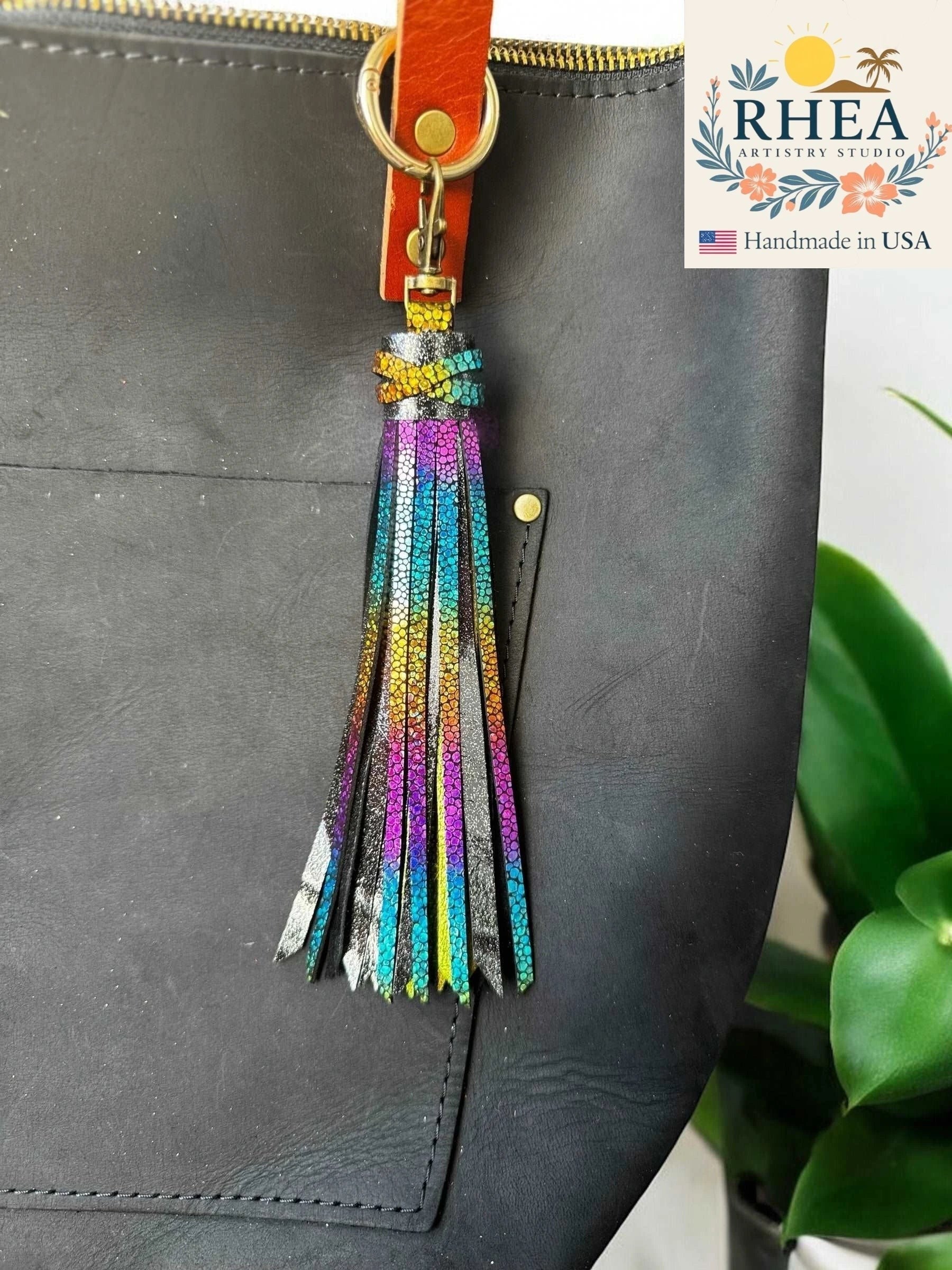 Rhea Artistry Studio handmade 7-inch rainbow chameleon leather tassel keychain with lobster clasp attached to a black bag.