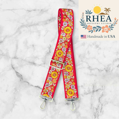 Rhea Artistry Studio red 2-inch wide strap with embroidered yellow, pink, and white flowers. Adjustable crossbody bag strap with brushed brass hardware.