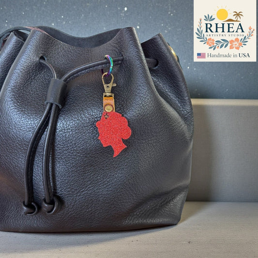 Rhea Artistry Studio red glitter profile silhouette charm attached to a black leather drawstring bag.