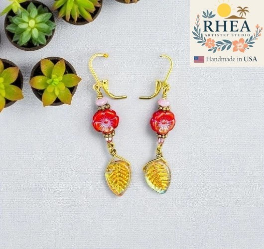 Rhea Artistry Studio red hibiscus floral earrings with pink bead accents and gold leaf drops.