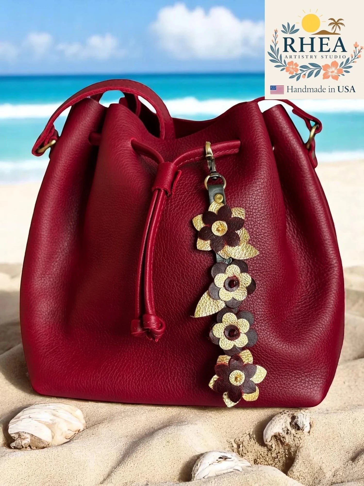 Rhea Artistry Studio deep red leather drawstring bucket bag with a floral leather charm featuring gold accents and Czech beads.