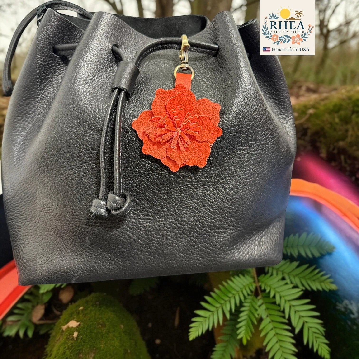 Rhea Artistry Studio red leather flower charm attached to a black leather drawstring bag.