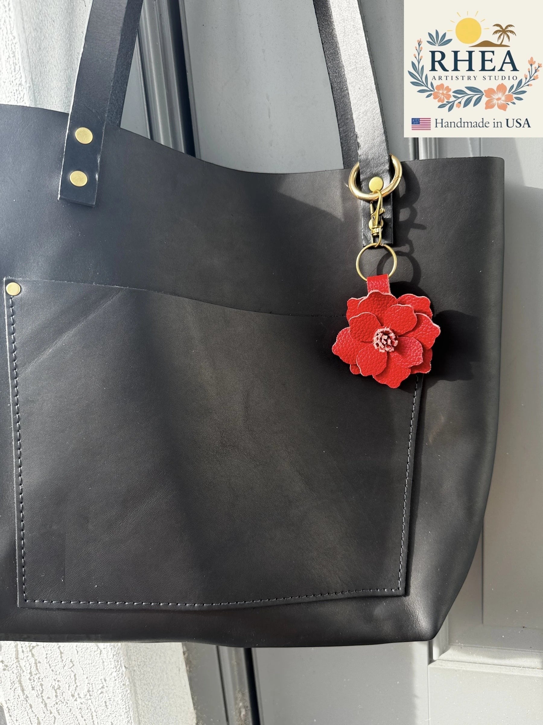 Rhea Artistry Studio red leather flower charm with detailed petals and stamen, attached to a black tote bag.
