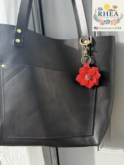 Rhea Artistry Studio red leather flower charm with detailed petals and stamen, attached to a black tote bag.