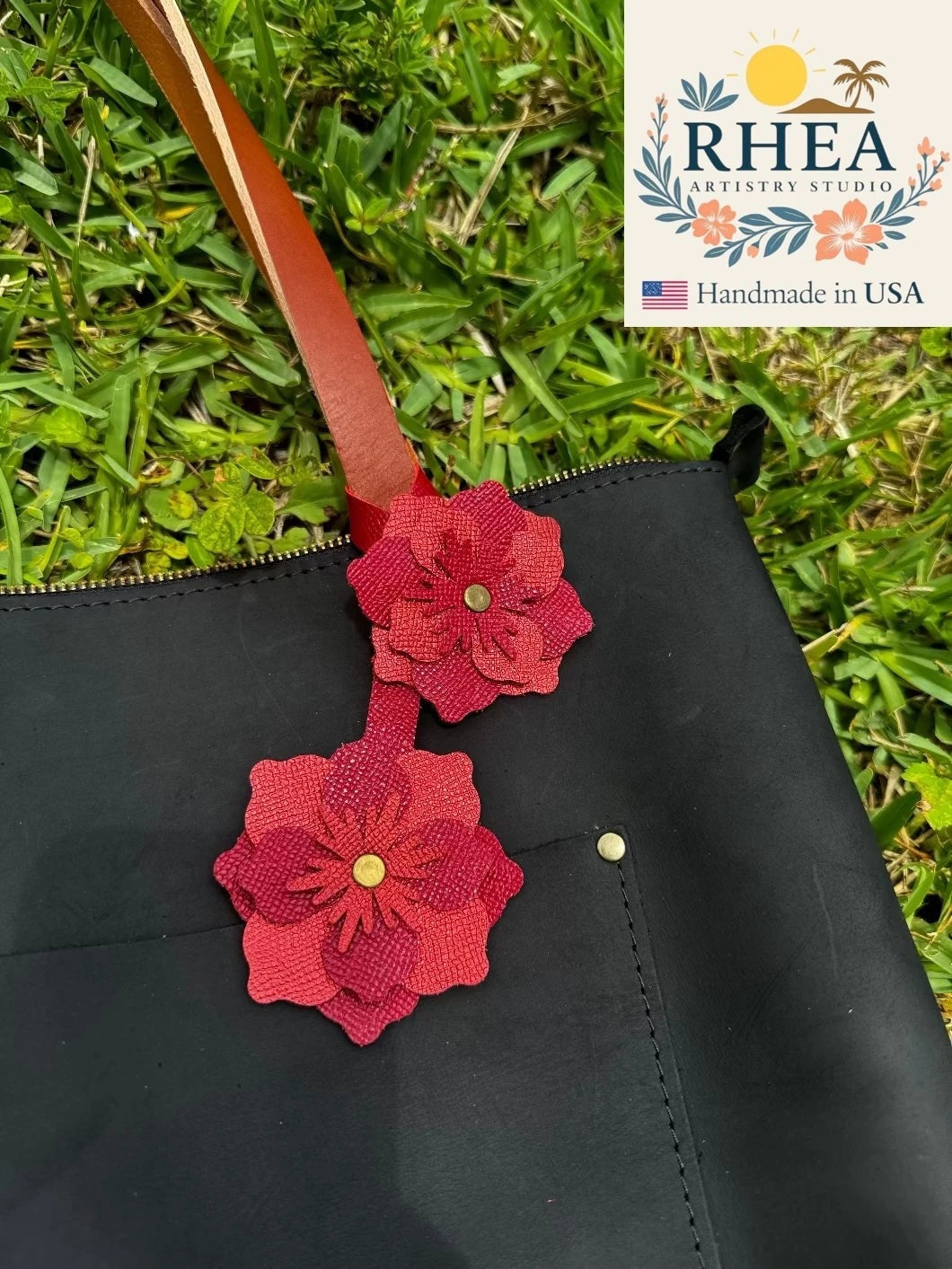 Rhea Artistry Studio double leather flower charm in red and brick red, attached to a black bag.