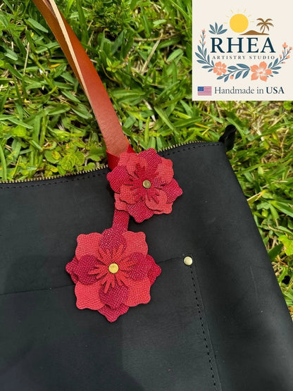 Rhea Artistry Studio double leather flower charm in red and brick red, attached to a black bag.