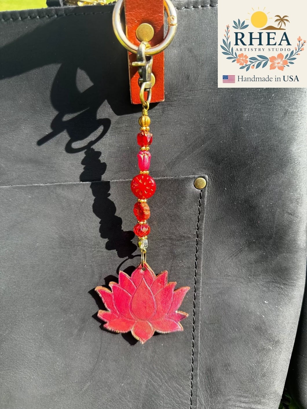Rhea Artistry Studio red leather lotus bloom charm with brass hardware and Czech glass beads, 6.5 inches long, attached to a black bag.