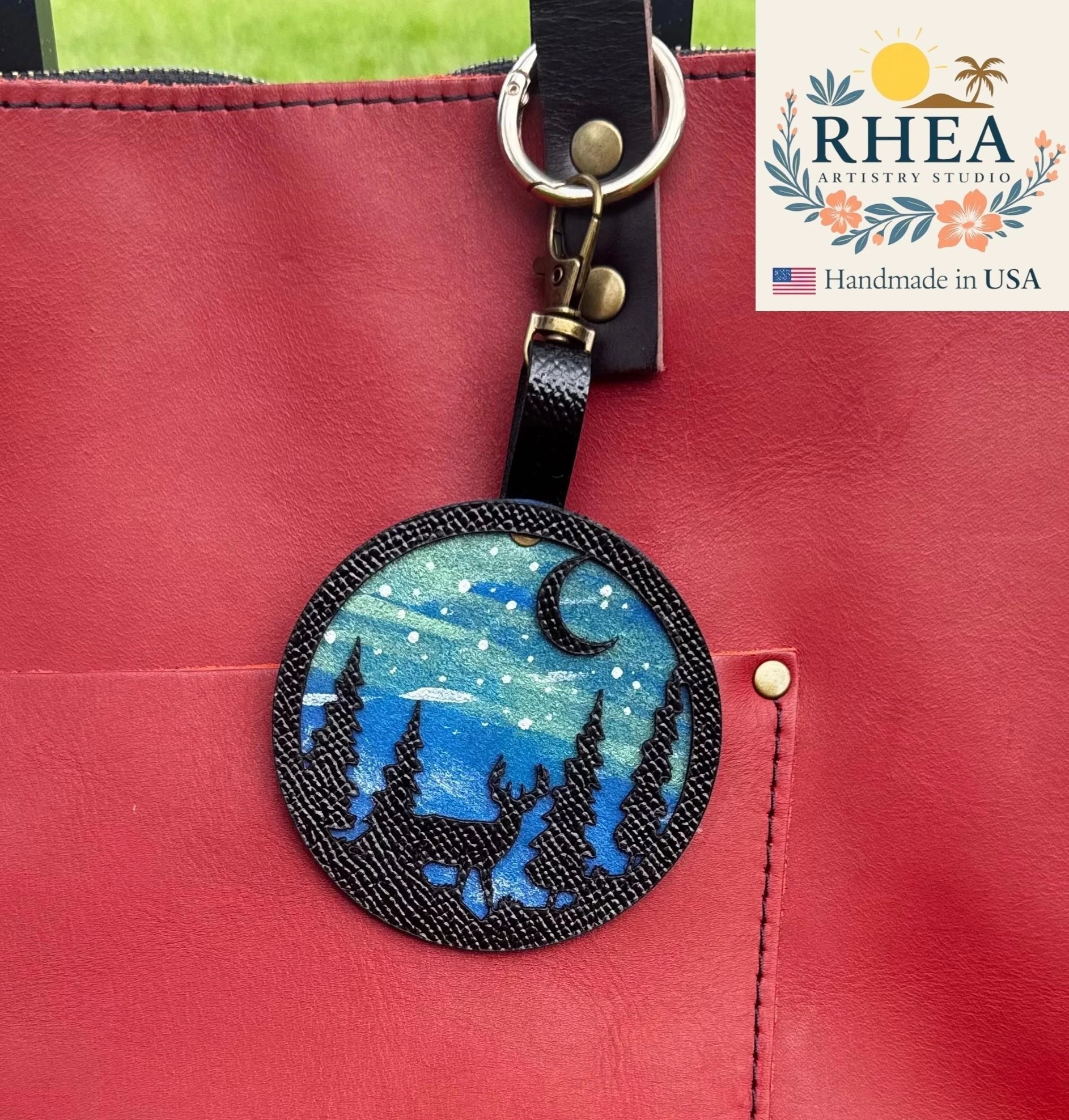 Rhea Artistry Studio hand-painted leather bag charm featuring a starry night sky with a deer and forest silhouette on vegetable-tanned leather.