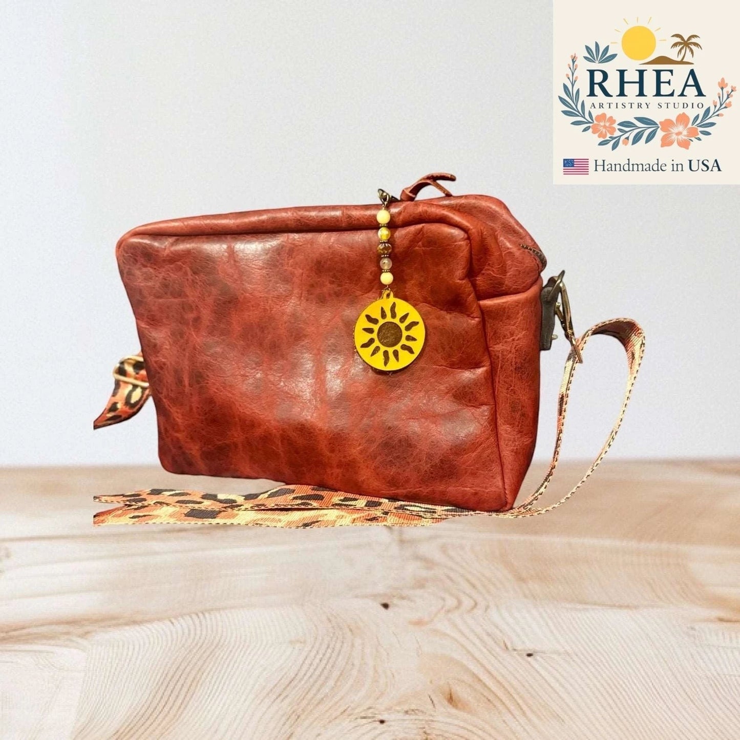 Rhea Artistry Studio handmade sun charm with yellow gemstone and Czech glass beads on a rustic brown leather crossbody bag.