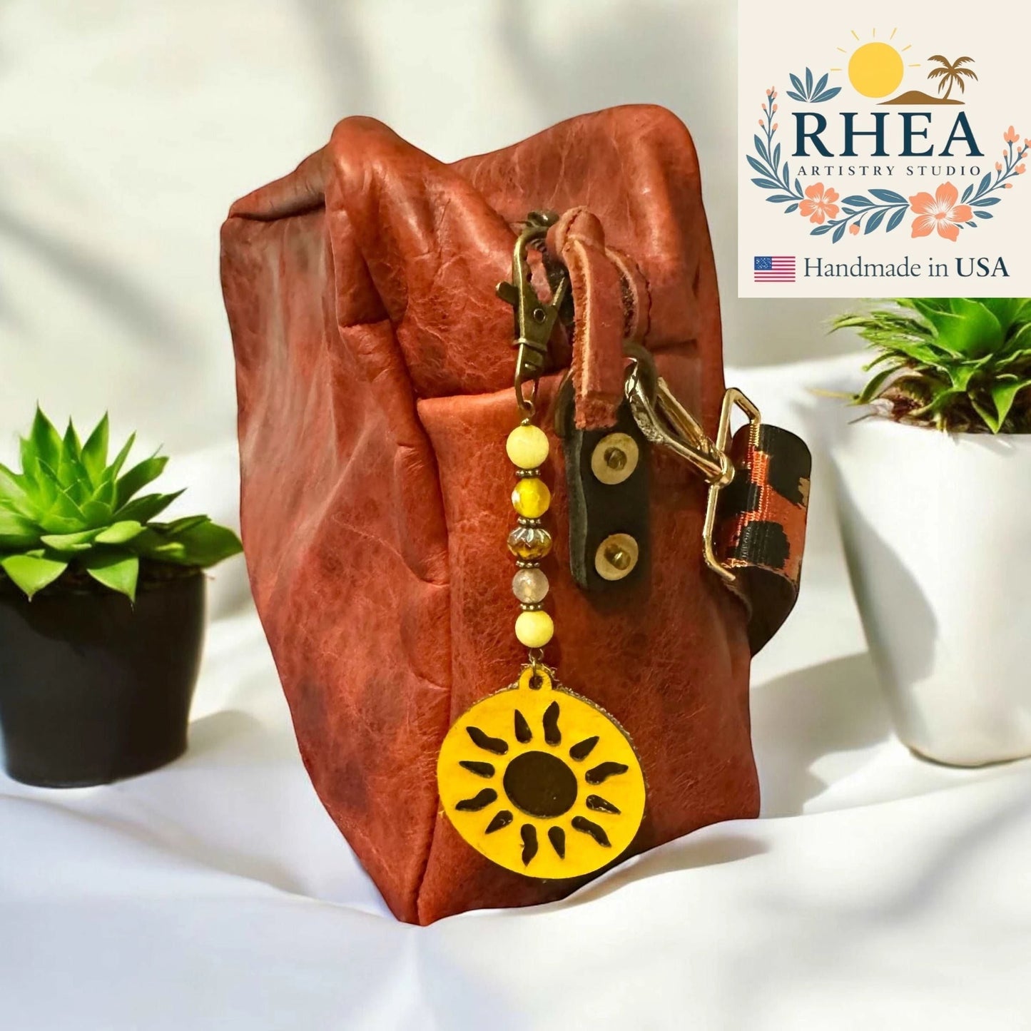 Rhea Artistry Studio handmade yellow sun charm with gemstone and Czech glass beads, attached to a rustic leather bag.