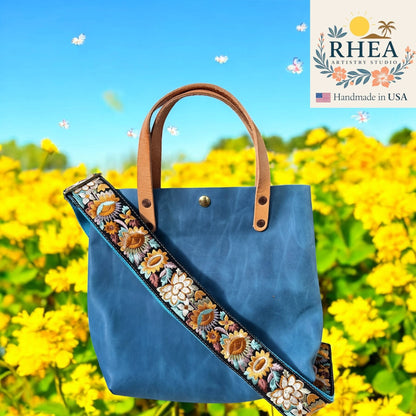 Rhea Artistry Studio blue leather tote bag with a 2-inch wide sunflower embroidered crossbody strap, adjustable and handmade.
