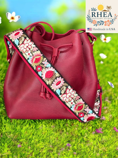 Rhea Artistry Studio red leather bucket bag with a 2-inch wide adjustable crossbody strap featuring vibrant sunflower embroidery.