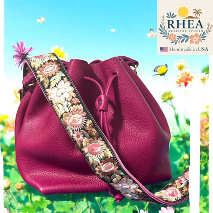 Rhea Artistry Studio 2-inch wide crossbody strap with vibrant floral embroidery in pinks and golds on a black background, attached to a magenta bucket bag.