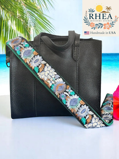 Rhea Artistry Studio 2-inch wide crossbody strap with embroidered sunflowers in blue, white, and brown on a black background with green trim.