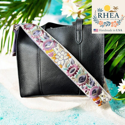 Rhea Artistry Studio 2-inch wide crossbody strap with vibrant floral embroidery in purple, yellow, and white on a black leather purse.