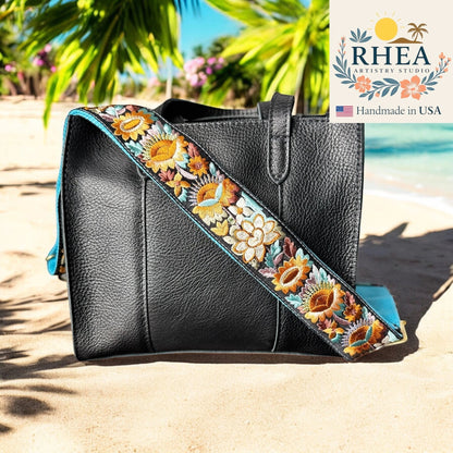 Rhea Artistry Studio black leather tote with a 2-inch wide sunflower embroidered strap featuring turquoise trim and brushed brass hardware.