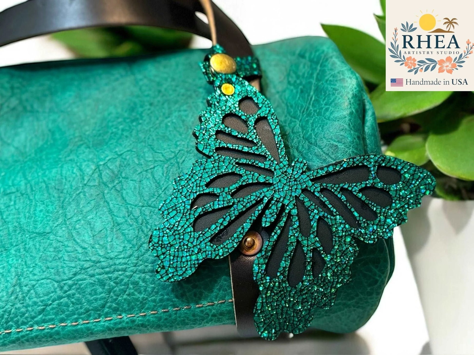 Rhea Artistry Studio teal leather butterfly charm with metallic iridescent finish and snap closure attached to a teal handbag.