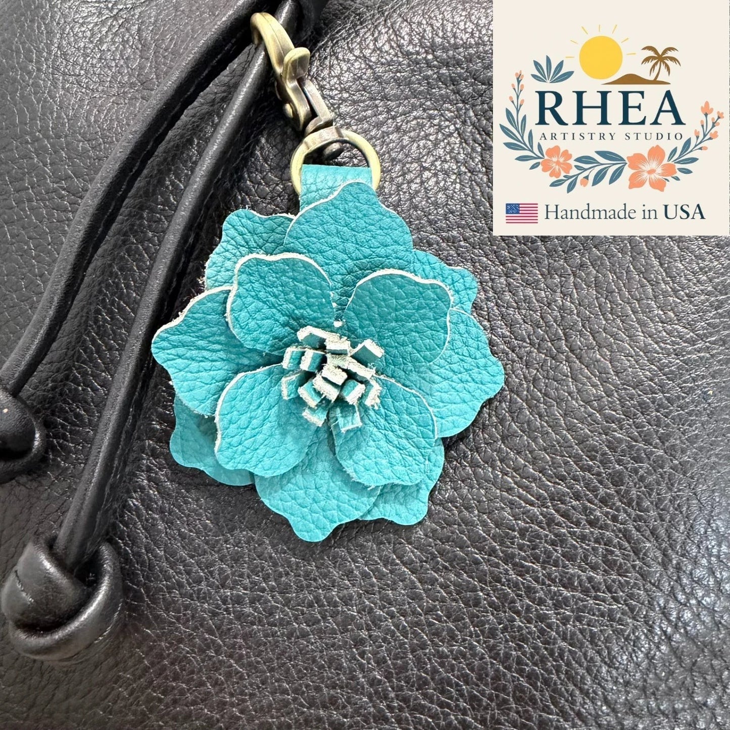 Rhea Artistry Studio teal blue leather flower charm attached to a black leather bag. Handcrafted floral accessory.